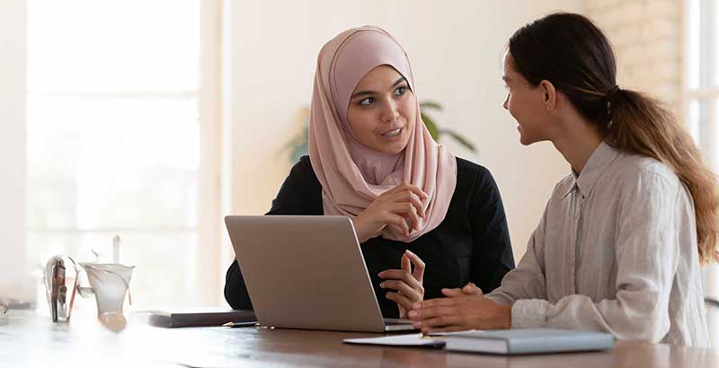 Two professional women discussing ideas together at a laptop during a leadership mentoring session
