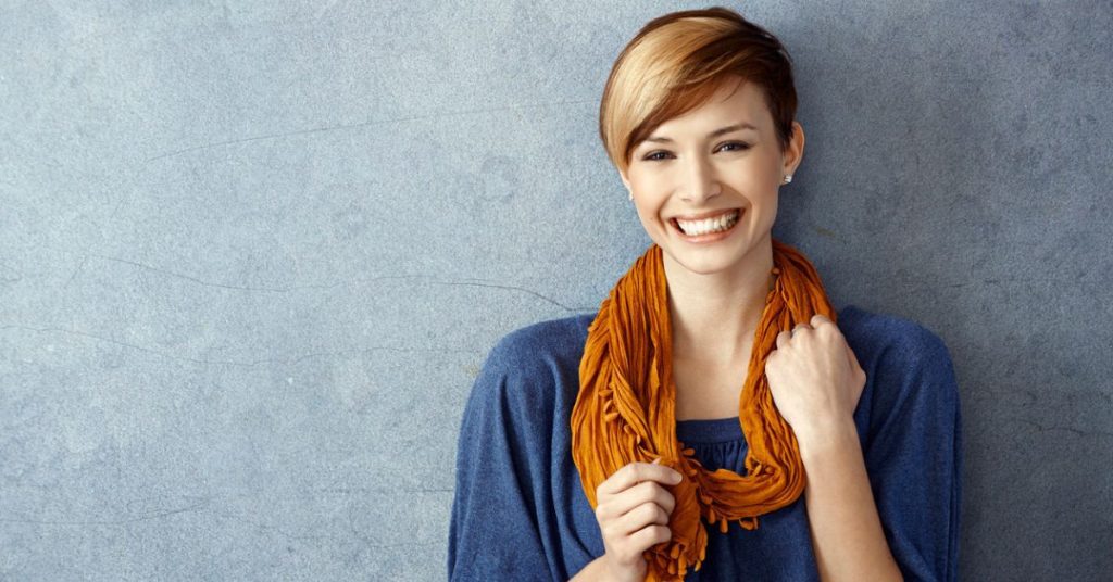 Confident woman smiling in a blue top and mustard scarf, symbolising the rise of modern female leadership styles.
