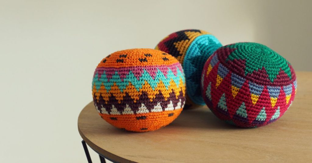 How Do You Celebrate Your Wins? | Women Leading Women Australia Three colourful woven juggling balls on a wooden table, representing balance, play, and celebrating success at work.