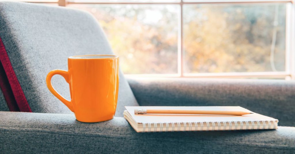 Quiet Quitting? Try This Instead | Women Leading Women Australia Bright orange mug and notebook on a sofa beside a sunlit window — symbolising rest and reflection instead of quiet quitting.