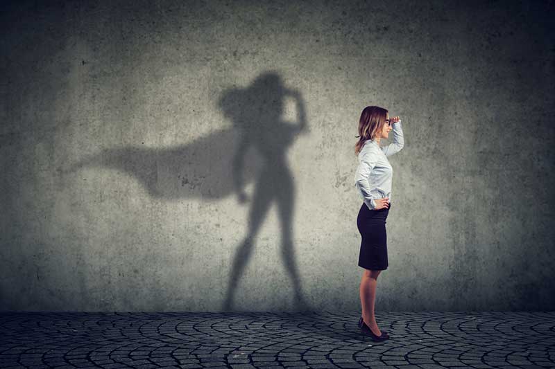 Executive woman standing confidently with her shadow as a superhero symbolising leadership growth.