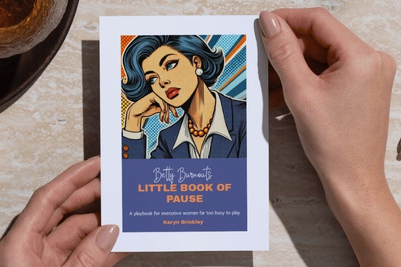 Close-up of hands holding the book Betty Burnout’s Little Book of Pause by Karyn Brinkley, a playbook for executive women who are too busy to play.