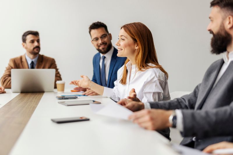 Professional woman speaking confidently in a meeting while colleagues listen attentively, representing strong communication and leadership presence.