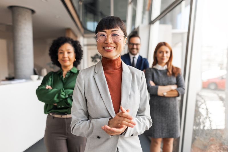 Professional woman smiling confidently with her team in a modern office, representing emotional mastery in leadership.
