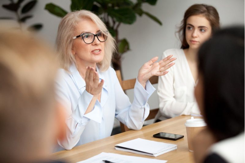 Senior female facilitator leading a discussion with executives around a table during a leadership workshop.