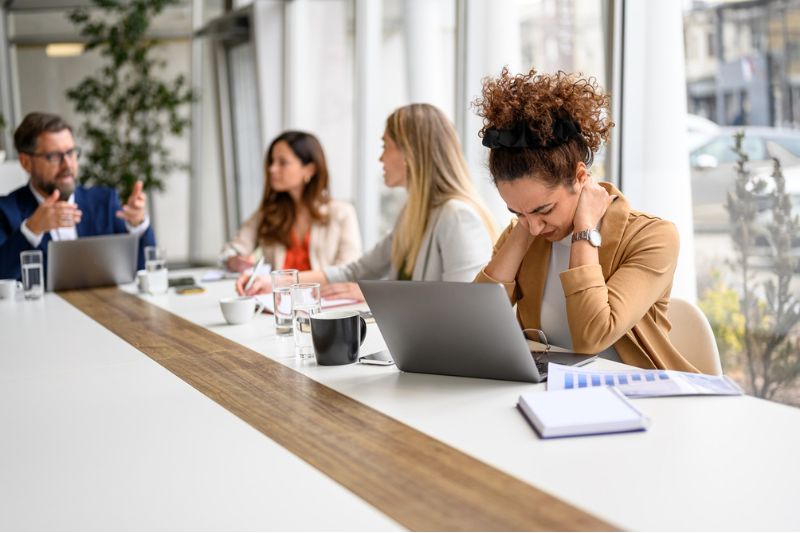 Businesswoman showing signs of tension during a board meeting, representing the impact of workplace burnout across leadership teams.