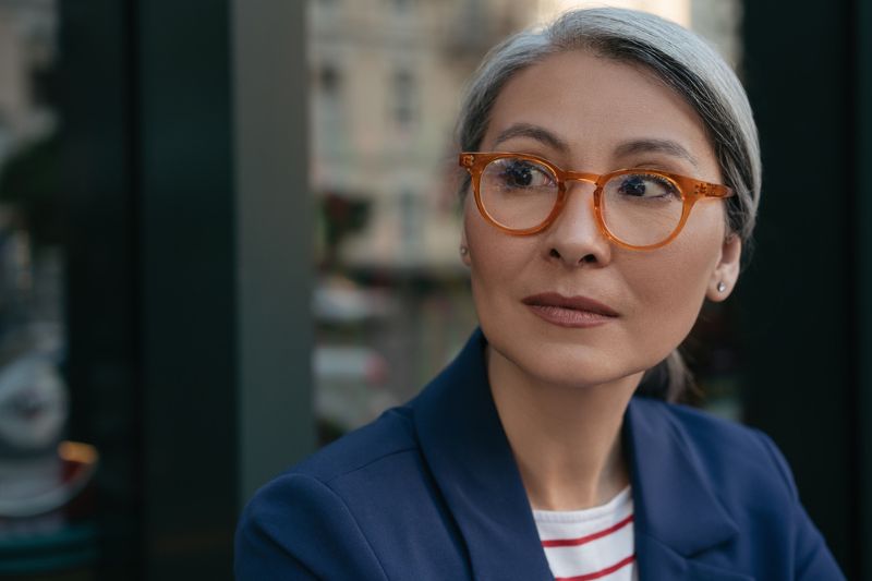 Thoughtful professional woman in glasses looking ahead with focus, representing strategic vision and clear decision-making in leadership.