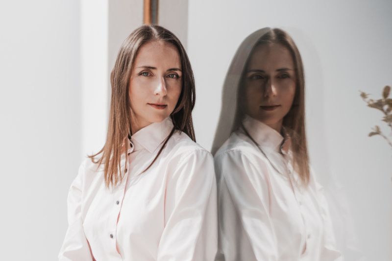 Professional woman standing beside her reflection in glass, symbolising introspection and overcoming self-doubt.
