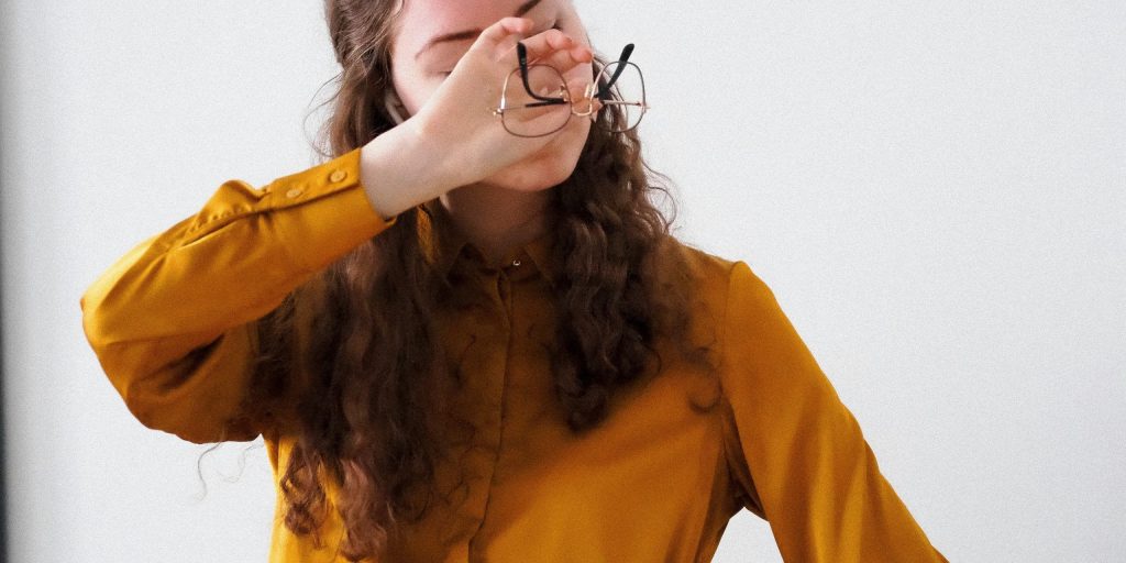 Executive woman removing her glasses in a moment of overwhelm, representing the emotional challenge of setting leadership boundaries